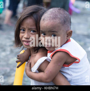 Das arme Mädchen mit emotionalen Lächeln versucht, obwohl Gegner. kümmert sich um ihren kleinen Bruder. Leben in der philippinischen Slum tapfer zu sein. Stockfoto