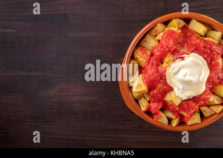 Ein overhead Nahaufnahme aus einer Schüssel Patatas Bravas, traditionelle spanische Teller Bratkartoffeln mit zwei Saucen, auf einem dunklen rustikalen Textur mit Kopie Raum Stockfoto