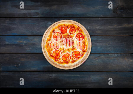 Pizza Margarita auf einem Stand aus Holz mit Tomatenscheiben auf einem dunklen Hintergrund. top View Center Ausrichtung. Stockfoto