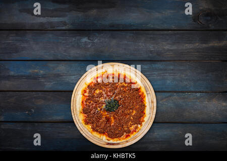 Leckere Pizza mit Hackfleisch auf einem Stand aus Holz auf einem dunklen Hintergrund. Draufsicht unten Ausrichtung. Stockfoto