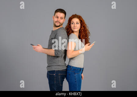 Ein schönes junges Paar Rücken an Rücken stehend, während halten und mit ihren smartphones Stockfoto