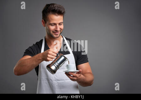 Ein junger Barista Mann lächelnd und gießen Kaffee aus einer Kaffeemaschine, einem coffeecup Stockfoto