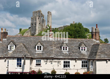 Die Ruinen von Corfe Castle, Devon steht auf dem Hügel mit Blick auf das Dorf gleichen Namens mit dem Greyhound Public House im Vordergrund. Stockfoto