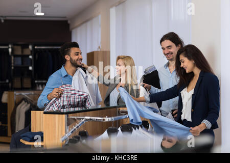 Geschäftsleute in Luxus Boutique Anzüge Hemden kaufen, zwei attraktive weibliche Verkäufer helfen Männer Kleidung zu wählen Stockfoto