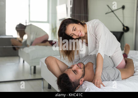 Paar umarmen, im Bett liegend, junge Frau sitzen auf Mann im Schlafzimmer Stockfoto