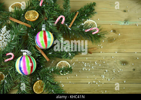 Weihnachten Farbe Bild von grünen Zweigen auf hölzernen Hintergrund mit Zimtstangen orange Fruchtschnitten und weißen Schneeflocken alle mit Schnee bestäubt Stockfoto