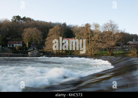 Lange Belichtung geschossen von einem Wasserfall im Winter. ein Dorf und einige Bäume bilden den Hintergrund dieser Winter Szene. Stockfoto