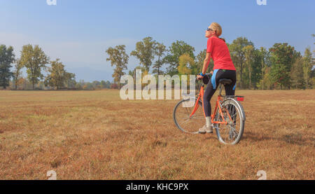 Eine Frau, die Übungen auf einem Fahrrad/einen gesunden Lebensstil einer 50 Jahre alten Frau üben Radfahren in einem Park Stockfoto