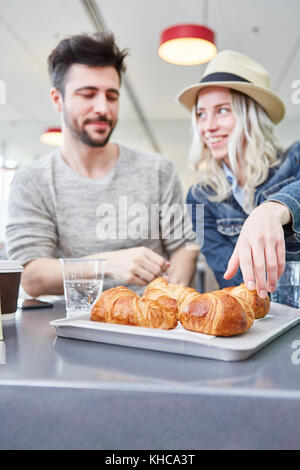 Junges Paar ist hungrig und zusammen zu essen Croissants im Bistro in der Shopping Mall Stockfoto