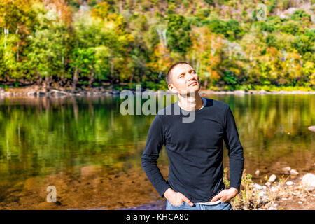 Nahaufnahme des Gesichts des jungen Mannes mit geschlossenen Augen meditieren Natur genießen mit friedlichen, ruhigen Fluss See während der sonnigen Herbsttag mit Reflexion Stockfoto