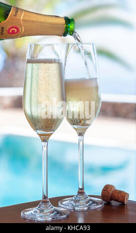 CODORNIU LUXUS LIFESTYLE CHAMPAGNER Gläser gießen der Spanischen Codorniu Cava brut Sekt Alfresco, mit luxuriösen Ferienhäuser Infinity Pool und Palmen im Hintergrund Stockfoto