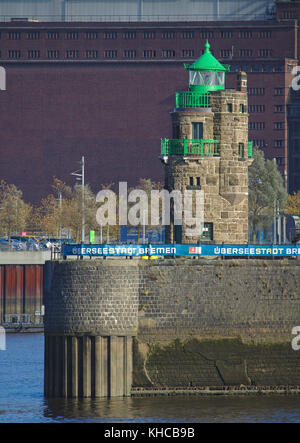 Bremen, Deutschland - 6. November 2017 - Leuchtturm am Hafeneingang auf einem Steinkai mit großem historischen Lagergebäude im Hintergrund Stockfoto