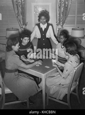 Eine Gruppe junger Kriegsarbeiterinnen wird gezeigt, wie sie ein Kartenspiel im Spielzimmer der Lucy D Slowe Residence Hall genießen, dem ersten von der Regierung errichteten Hotel für afroamerikanische Kriegsarbeiterinnen, Washington, DC, 1942. Aus der New York Public Library. Stockfoto