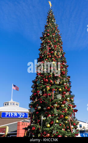 THANKSGIVING Weihnachtsbaum vor dem beliebten Touristenkomplex Pier 39 mit Stars and Stripes US-Flagge, die Embarcadero San Francisco, Kalifornien, USA, fliegt Stockfoto