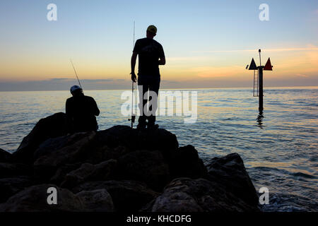 Fischer in Silhouette in der Abenddämmerung auf Felsen am Venice Beach Stockfoto