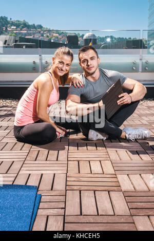 Junge Erwachsene Personal Fitness Trainer (Coach), die die Ergebnisse und Leistungen zu seinen jungen weiblichen Client auf dem Dach des Gebäudes im Stadtzentrum. Stockfoto