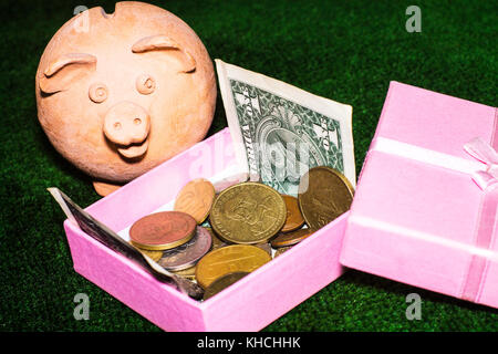 Steuer Tag. Piggy Bank mit einem rosafarbenen Geschenkbox und Geld gegen den grünen Teppich Hintergrund. Stockfoto