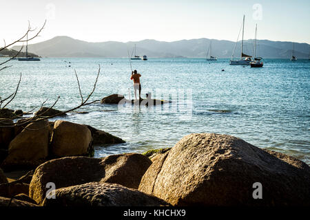 Mann angeln auf einem Felsen an der felsigen Küste in Jurere Beach. Florianopolis, Santa Catarina, Brasilien. Stockfoto