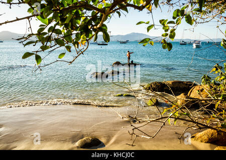 Mann angeln auf einem Felsen an der felsigen Küste in Jurere Beach. Florianopolis, Santa Catarina, Brasilien. Stockfoto