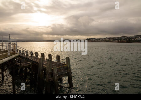 Sonnenuntergang über Torbay von Torquay Pier mit einem Bootssteg im Vordergrund. Dunkle Wolken mit Sturm nähert. Stockfoto