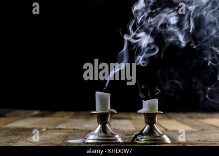 Durchgebrannte Kerzen in silbernen Kerzenständern mit geräuchertem Wick. Rauch aus einem Docht auf einem schwarzen Hintergrund. Holztisch Stockfoto