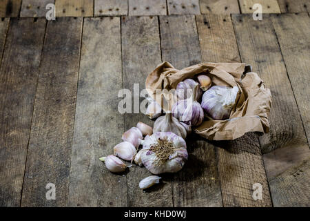Knoblauch in einem zerknitterten Papier auf einem Holztisch. Tisch mit Knoblauch in Papiertüte. schwarzer Hintergrund Stockfoto