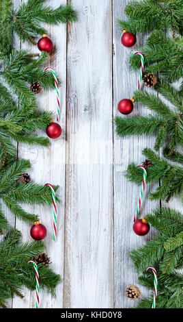 Christmas tree branches, Zuckerstangen und roten Verzierungen bilden vertikale Grenzen auf rustikalen weißem Holz Stockfoto