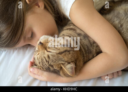 Kaukasische Mädchen umarmt Katze auf Bett Stockfoto