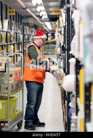 Die Mitarbeiter machen sich auf den Weg durch die Gänge und sammeln Gegenstände, bevor sie sie in die Versandhalle vor Ort schicken, wo sie in einem der größten britischen Amazon-Lagerhäuser in Dunfermline, Fife, verpackt werden. Der Online-Shopping-Riese bereitet sich auf den Weihnachtsrausch und die bevorstehenden Black Friday-Verkäufe vor. Stockfoto