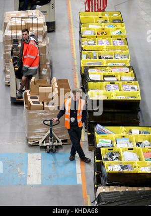 Die Mitarbeiter machen sich auf den Weg durch die Gänge und sammeln Gegenstände, bevor sie sie in die Versandhalle vor Ort schicken, wo sie in einem der größten britischen Amazon-Lagerhäuser in Dunfermline, Fife, verpackt werden. Der Online-Shopping-Riese bereitet sich auf den Weihnachtsrausch und die bevorstehenden Black Friday-Verkäufe vor. Stockfoto