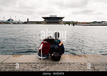 Ein paar der jungen Menschen umarmt sitzen mit Blick auf die waterfr Stockfoto