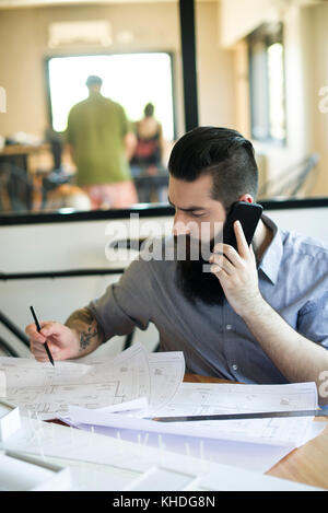Mann mit Handy und Blueprints im Büro Stockfoto