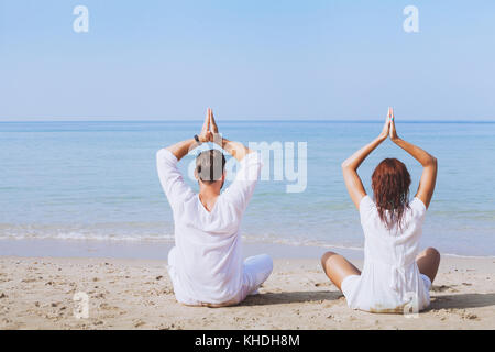 Yoga am Strand, zwei Menschen in weißen Kleidern üben Meditation, gesunden Lebensstil Hintergrund Stockfoto