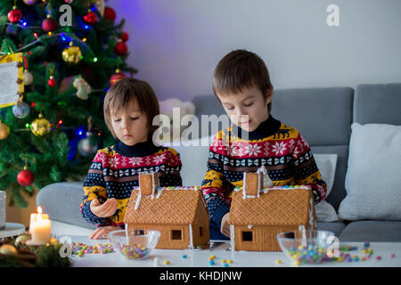 Adorable Vorschule Kinder, junge Brüder, dekorieren Lebkuchenhäuser für Weihnachten zu Hause, Weihnachtsbaum hinter Ihnen, Advent Kerzen auf den Tabl Stockfoto