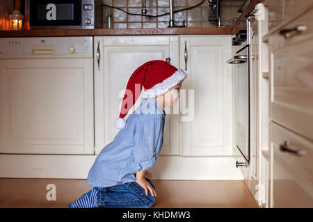 Neugierige kleine Junge, gerade Lebkuchen Cookies im Ofen backen für Weihnachten Stockfoto