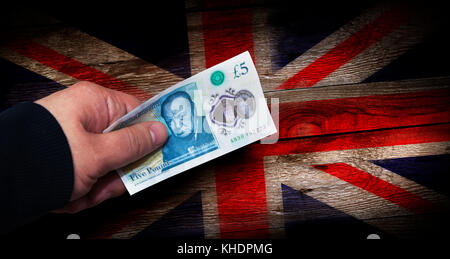 Geld englisch fünf Pfund Hinweis in der Hand eines Mannes auf einem grunge Britische Flagge auf einer hölzernen Oberfläche Stockfoto