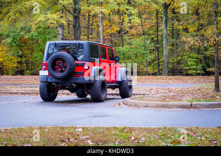 Red 4wd Geländewagen auf einem Parkplatz im Herbst Wald geparkt von der Rückseite mit breiten Reifen und Ersatzteile auf der Rückseite montiert gesehen Stockfoto