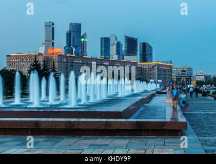 Menschen zu Fuß entlang der Brunnen der Poklonnaya Hügel mit Kutusovkij Prospekt und der Moscow International Business Center (MIBC) im Hintergrund. Stockfoto