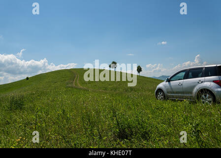 Blick von der Straße zu den Wiesen mit Blumen und ein Auto auf ein Hintergrund der Hügel und blauer Himmel mit Wolken Stockfoto