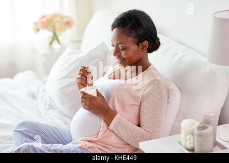 Schwangere Frau isst Joghurt im Bett Stockfoto