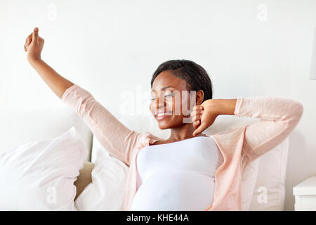 Glücklich schwanger afrikanische Frau Stretching im Bett Stockfoto