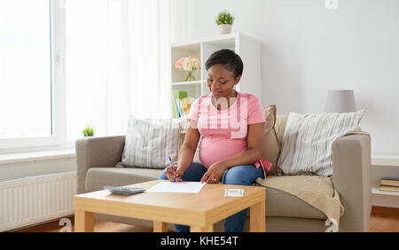 Schwangere Frau mit Rechnungen und Geld zu Hause Stockfoto