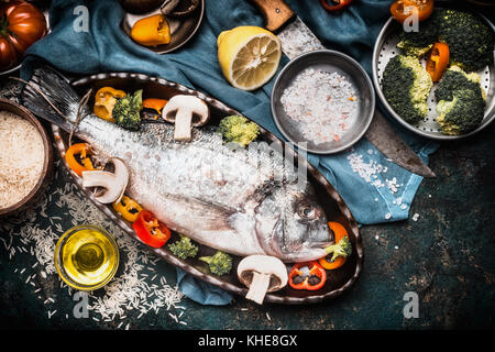 Fisch kochen Vorbereitung mit Dorado der Unterstützung in Form von Fisch mit gesundes Gemüse auf dunklen rustikalen Hintergrund mit Zutaten, oben Stockfoto