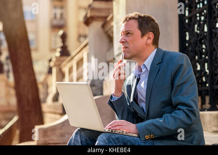 Ein mittleres Alter Geschäftsmann Standortwahl auf der Treppe mit einem Laptop und ein Handy in der Hand und Denken Stockfoto