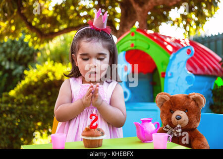 Baby Kleinkind Mädchen im Freien zweiten Geburtstag händeklatschen am Kuchen mit Teddy Bär als bester Freund, Playhouse und Kaffee. rosa Kleid und Krone. Stockfoto