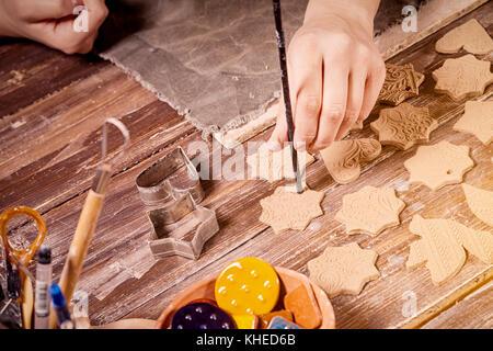 Potter macht viel Weihnachten Spielzeug, Weihnachtsbäume aus brauner Ton, in der Form von Herzen, Sterne, Bären, Schmetterlinge, Vögel und andere auf einem Holz Stockfoto