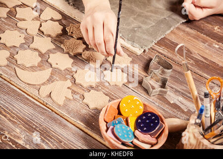 Potter macht viel Weihnachten Spielzeug, Weihnachtsbäume aus brauner Ton, in der Form von Herzen, Sterne, Bären, Schmetterlinge, Vögel und andere auf einem Holz Stockfoto