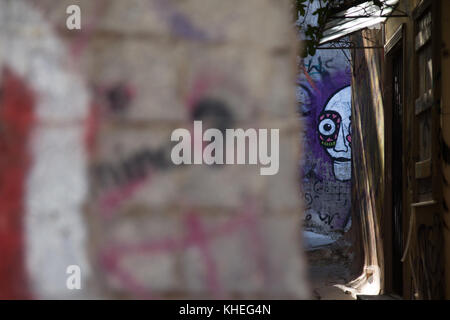 Graffiti eines gruseligen Gesichts durch eine Öffnung in einer kleinen Straße in der Plaka-Region in Athen, Griechenland Stockfoto