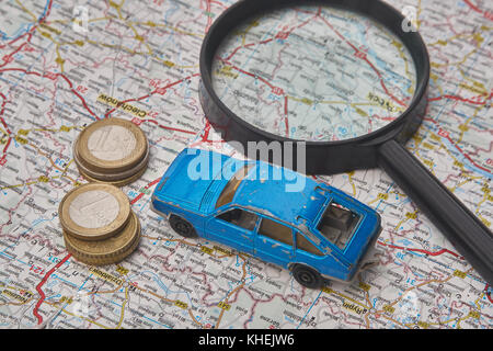 Spielzeugauto und Euro-Münzen, die mit einer Lupe auf einer Karte liegen. Stockfoto
