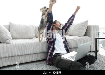 Happy Guy frohlockt mit seinem Hund sitzt in der Nähe der Couch im Wohnzimmer. Stockfoto